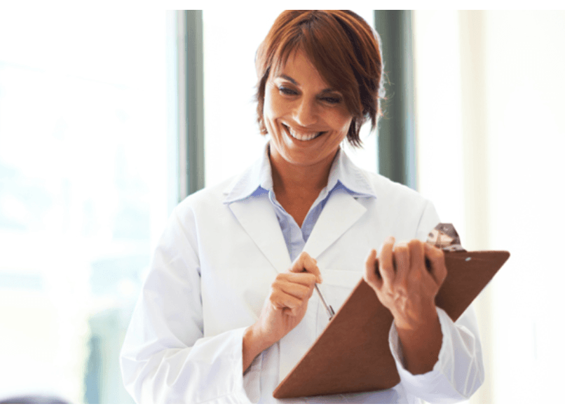 A doctor smiling as she writes on a clipboard
